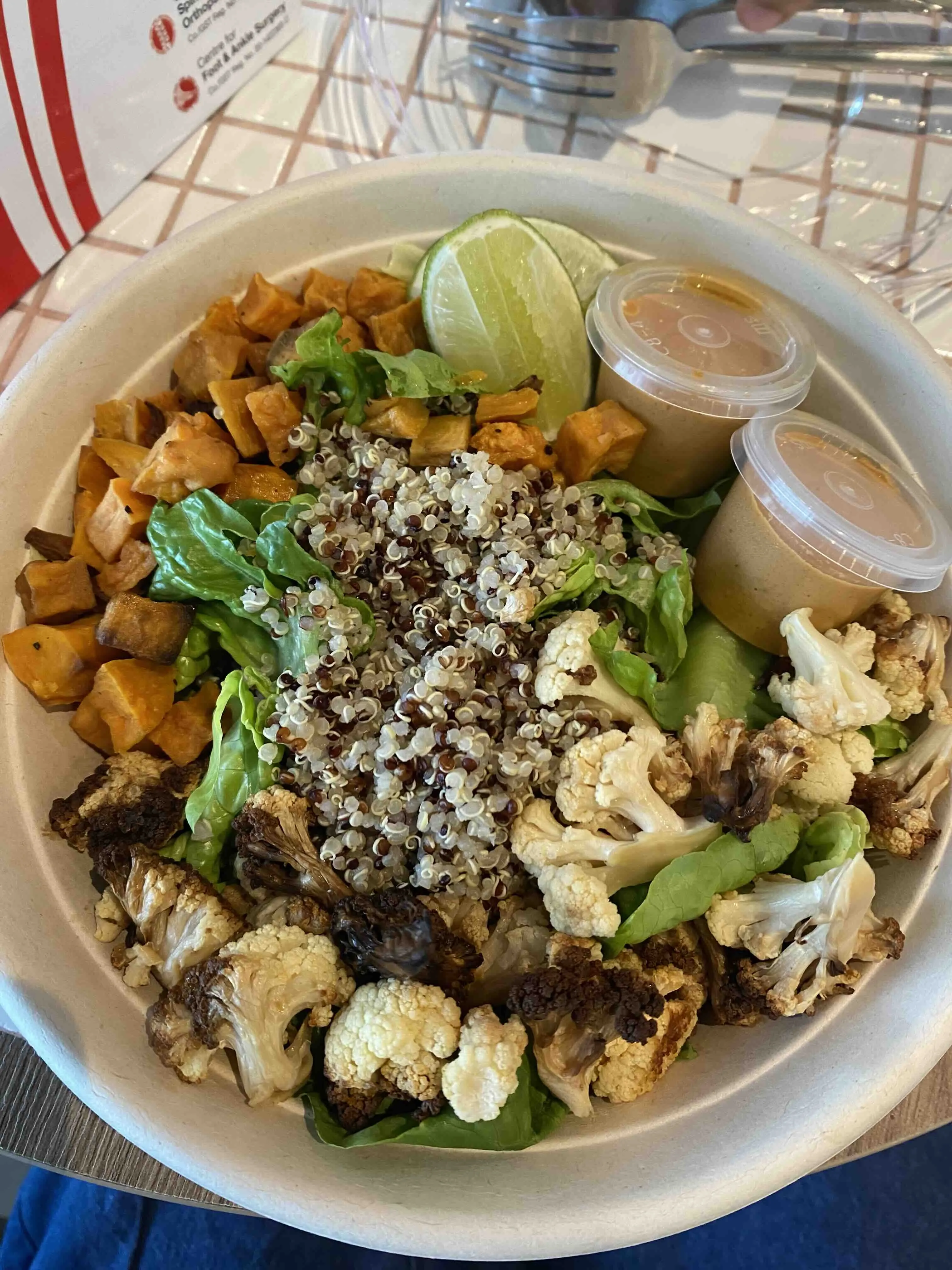 Healthy bowl consisting of cauliflower, salad greens, quinoa, tofu and seseme / tahini sauce